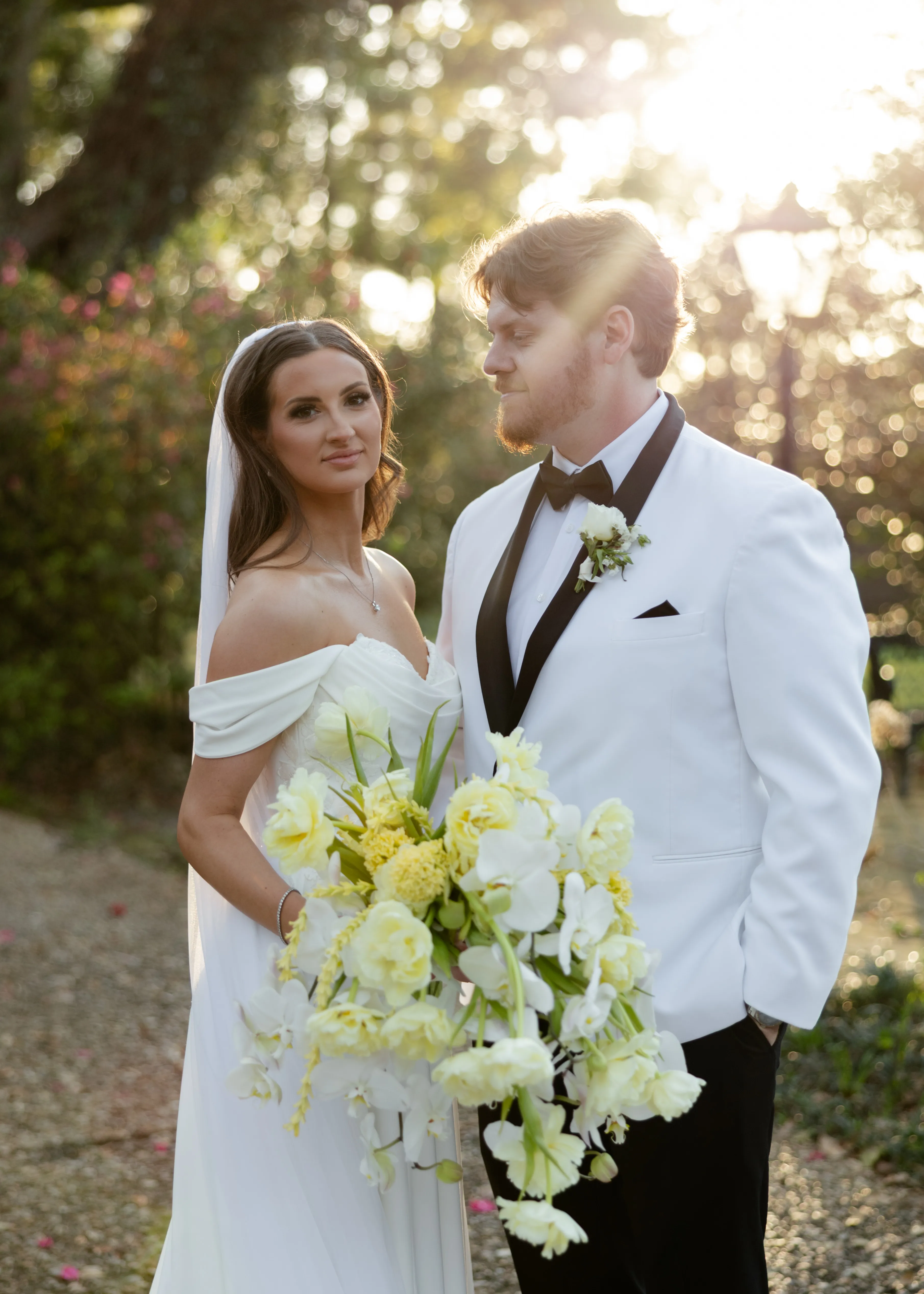 A couple standing close together in warm evening light, the groom in a white dinner jacket